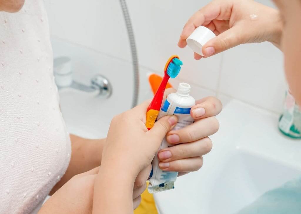 Parent teaching a child how to brush with kids toothpaste.